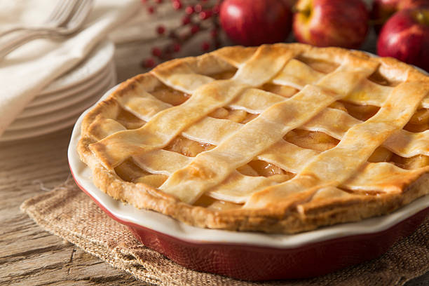 Apple Pie A lattice apple pie.  The apple pie is set in a fall scene with apples, dessert plates, forks, and seasonal decoration.  The pie is set on a rustic farm table with burlap textured hot pad.  This image could be used to illustrate:  Baking, Fall, Autumn, Thanksgiving, Apple pie, holiday desserts, holiday recipes, etc apple pie photos stock pictures, royalty-free photos & images
