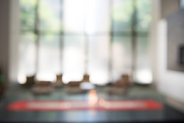 A blurry photograph of a modern corporate building lobby area background.  The back wall is primarily windows with daylight coming through.