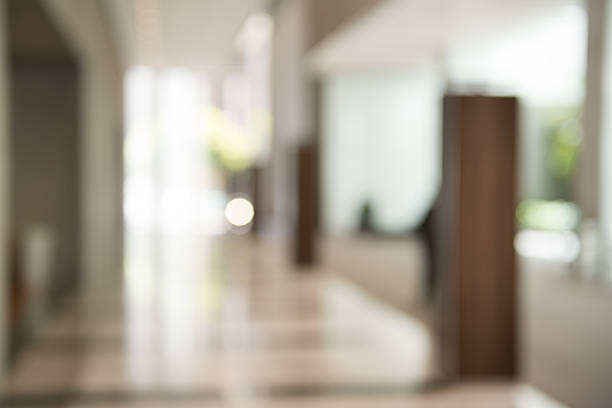 A blurry photograph of a modern corporate building lobby area background.  The back wall is primarily windows with daylight coming through.