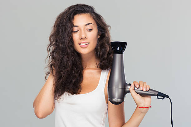 Smiling young woman holding hairdryer Smiling young woman holding hairdryer over gray background fen photos stock pictures, royalty-free photos & images