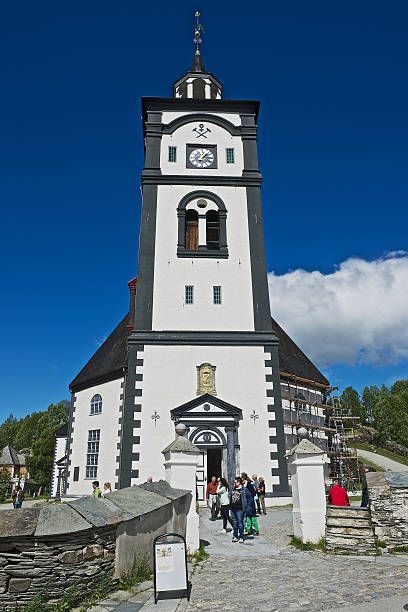 Tourists walk in front of the church in Roros, Norway. Roros, Norway - June 24, 2013: Unidentified tourists walk in front of the Roros church and bell tower in Roros, Norway. Roros mining town is declared a UNESCO World Heritage site. roros mining city stock pictures, royalty-free photos & images