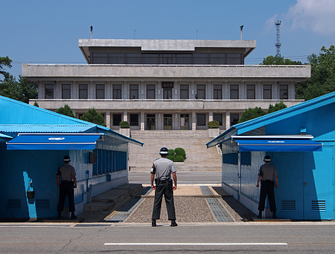 Panmunjeom, South Korea - June 14, 2014: South Korean soldiers stand guard - facing a single North Korean soldier - at the Joint Security Area in the Demilitarized Zone. The blue buildings are half in North Korea, half in South Korea. The building in the background is Panmun Hall in North Korea.
