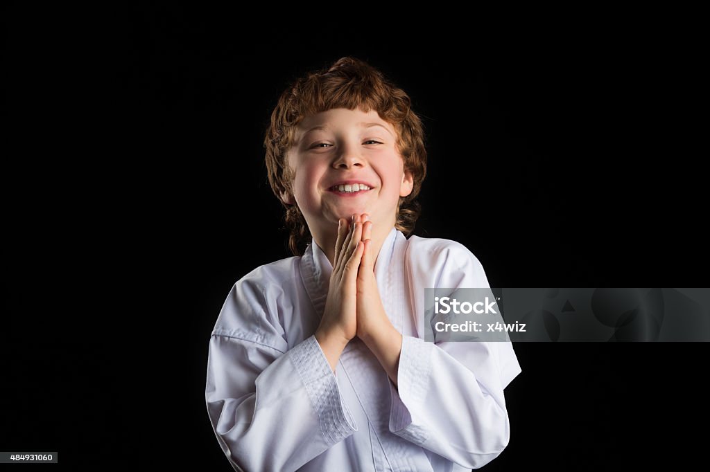 Smiling karate boy in white kimono isolated on black background Smiling redhead caucasian karate boy in white kimono isolated on black background 2015 Stock Photo