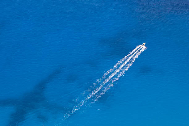 Motorboat Floats in the Sea High view aerial image of powerboat floating in a turquoise blue sea water. The boat is moving diagonally through the frame of the image. racing boat photos stock pictures, royalty-free photos & images