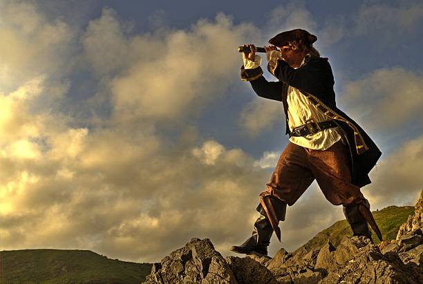 pirata standing on rocks mirando a través de su catalejo - espadachín fotografías e imágenes de stock