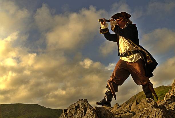 pirate standing on rocks looking through his telescope stock photo