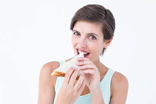 Happy brunette eating sandwich on white background
