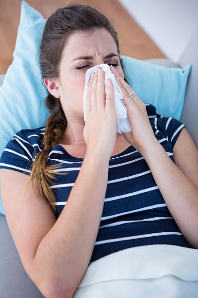 istock Sick woman blowing her nose lying on couch 484983690