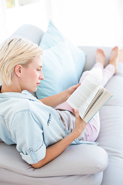 istock Pretty blonde woman reading a book on the couch 484987864