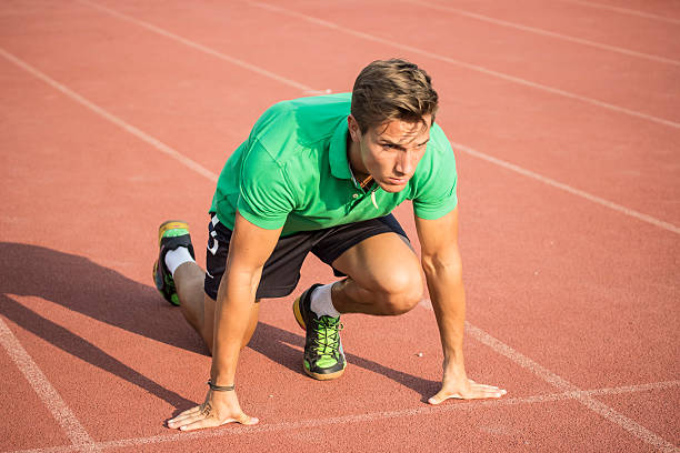 istock Male sprinter in clothes at start position, on red track. 485002686