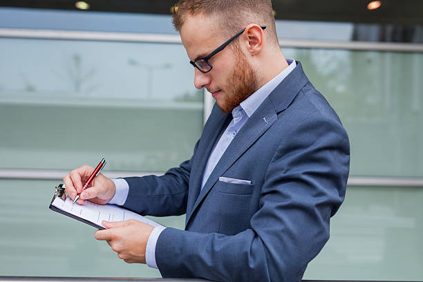 istock Young businessman with beard standing in front of office block. 485005464