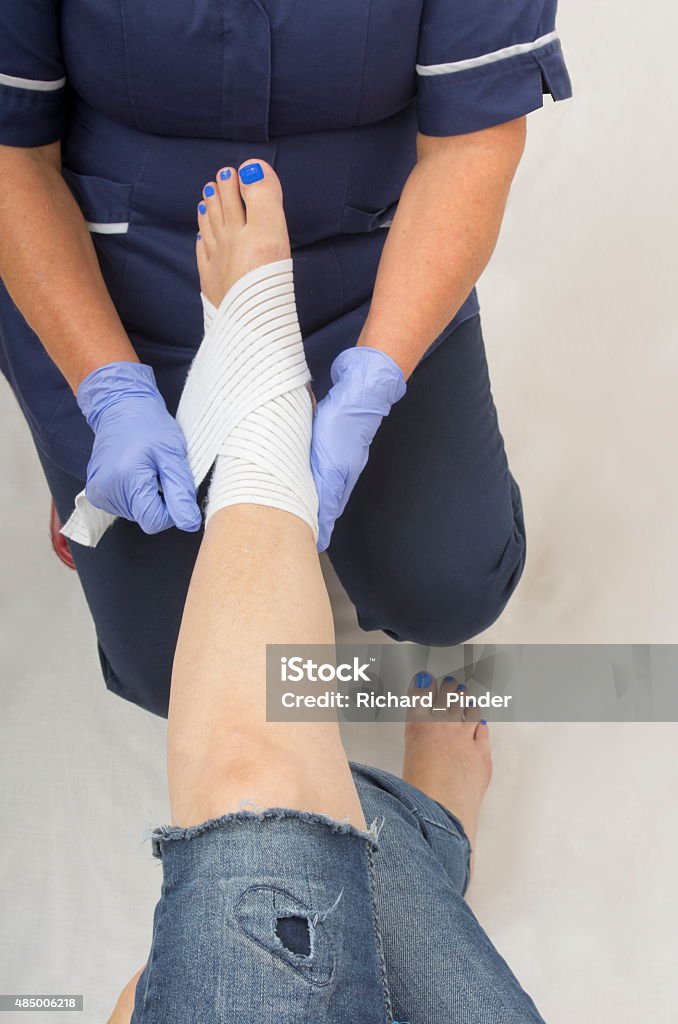 Ladies injured ankle being dressed by a nurse A nurse dressing a ladies ankle with an elasticated support bandage. 2015 Stock Photo