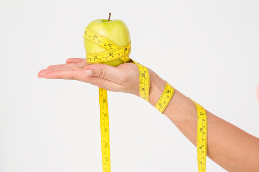 Woman holding apple with measuring tape on white background