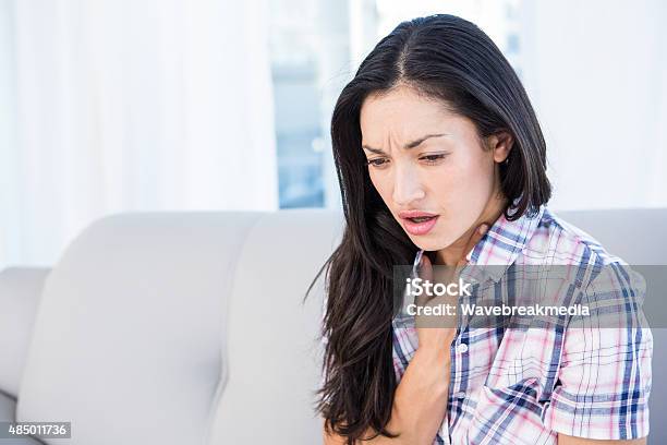 Pretty Brunette Coughing On Couch Stock Photo - Download Image Now - Coughing, Domestic Life, 2015