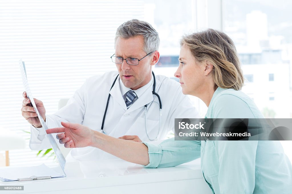 Doctor having conversation with his patient and holding xray Doctor having conversation with his patient and holding xray in medical office 2015 Stock Photo