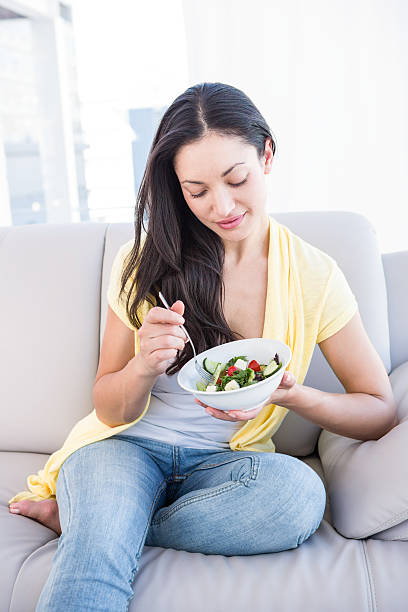 istock Pretty brunette eating salad on couch 485012942