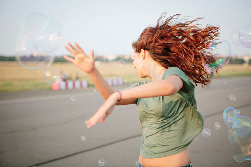 young woman has fun with soap bubbles, flying long hair, motion