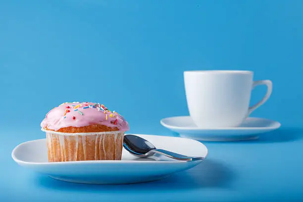 Colorful muffin on saucer. Blue plain background