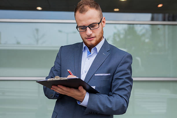 istock Young businessman with beard standing in front of office block. 485023422
