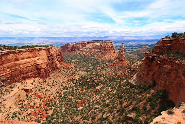 A mid-July landscape in Grand Junction, Colorado. The Independence Monument towers in the background, and in the distance are beautiful mountain ranges. These bright red rock formations were formed by erosion, and this monolith is the remnant standing in the middle of what used to be a long wall of rock.