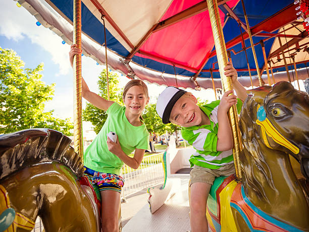 Cute kids having fun riding on a colorful carnival carousel Two cute kids enjoying a ride on a fun carnival carousel. A happy girl and boy are Smiling and having fun together at the summer carnival fairground ride stock pictures, royalty-free photos & images