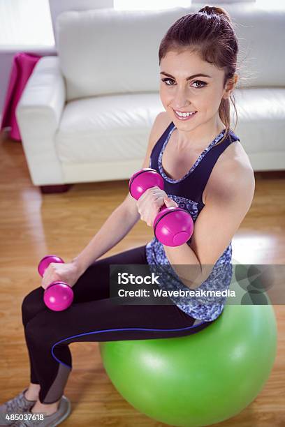 Fit Woman Lifting Dumbbells On Exercise Ball Stock Photo - Download Image Now - 20-24 Years, 20-29 Years, 2015