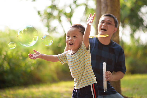 アジアの子供シャボン玉で遊ぶ父 - bubble wand child blowing asian ethnicity ストックフォトと画像