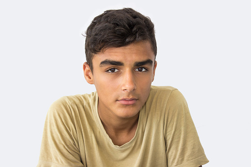 Teenage boy looking at camera with blank expression isolated on white. Taken in studio isolated on white and developed from Raw format. Horizontal shot. Boy staring to camera. Wearing casual clothing - t-shirt - .
