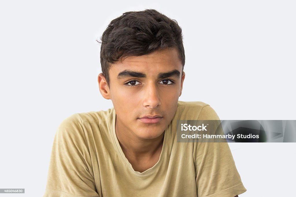 Teenage boy looking at camera with blank expression Teenage boy looking at camera with blank expression isolated on white. Taken in studio isolated on white and developed from Raw format. Horizontal shot. Boy staring to camera. Wearing casual clothing - t-shirt - . Teenage Boys Stock Photo