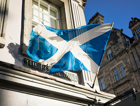 A weathered Scottish Saltire flag blowing in the wind on Edinburgh's historic Royal Mile.