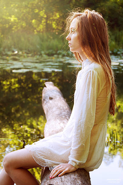 istock Redhead woman sitting on a tree bark near river 485057820