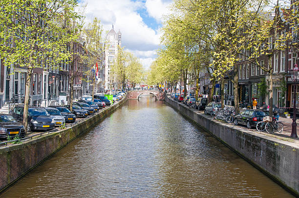 амстердам-канал с парковать автомобили вдоль берега. нидерланды. - europe sunlight river sun стоковые фото и изображения