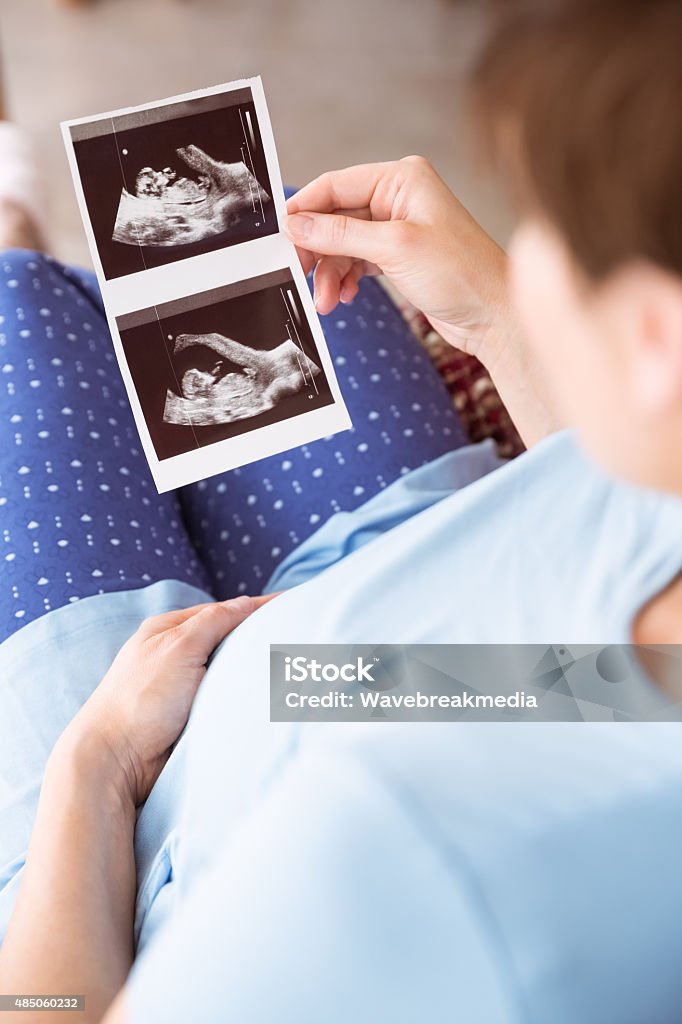 Pregnant woman looking at ultrasound scans Pregnant woman looking at ultrasound scans at home in the living room 2015 Stock Photo