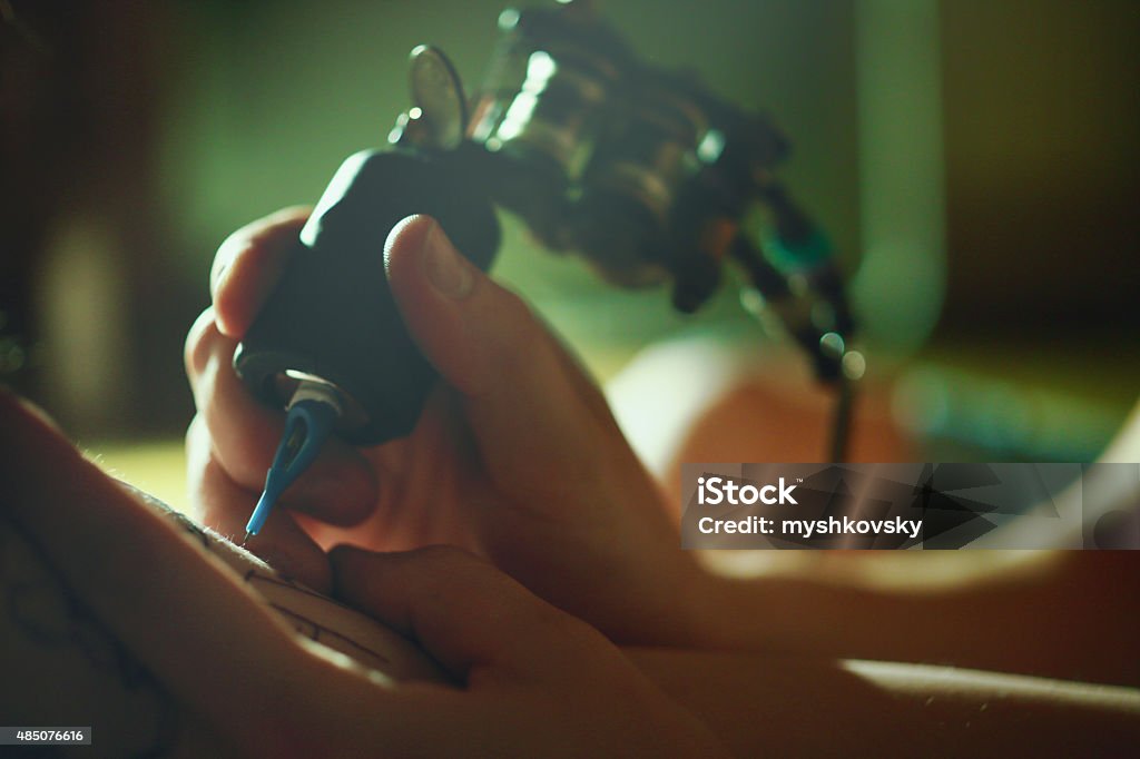 Tattoo master tattooing on the a girl arm. Tattoo Machine Stock Photo