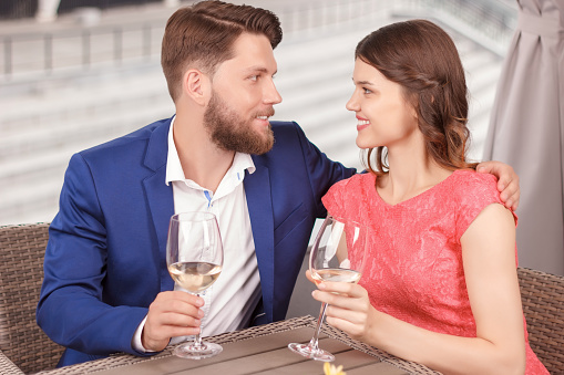 Slightly embracing. Young handsome man and pretty woman with glasses of wine embracing and looking at each other in restaurant.
