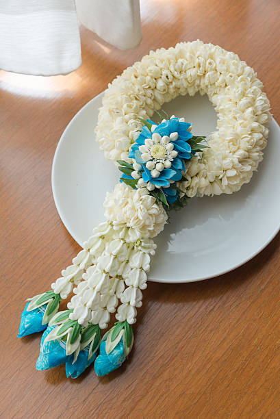 Jasmine garland decorated with blue roses Handmade jasmine garland decorated with blue roses locating on a white plate nearby the window. It is often use for praying and budhist customs at the temple. Jasmine garland is a Thai traditional way of flower arrangement. jasmine flower bouquet stock pictures, royalty-free photos & images