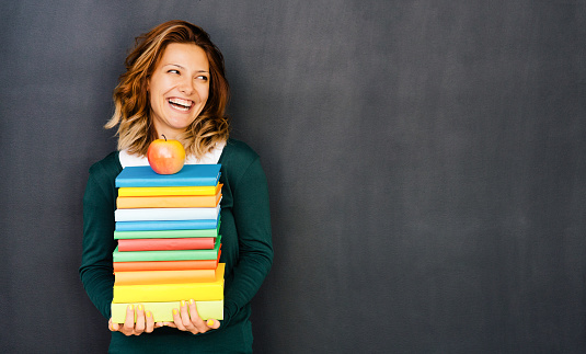 Young girl holding colorful books in front of a blackboard.