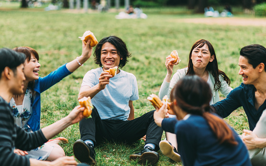 Japanese teenagers eating some fast food outside in the park. There is a lovely sunny day. The food seem delicious and they seem very happy.