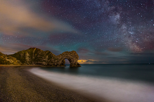 A night photograph taken at Durdle Door in Dorset. One of the most recognizable landmark in the UK. The photograph is taken at the waters edge and shows crashing waves, curve of the beach and the famous arch way. You can also see the Milkway.