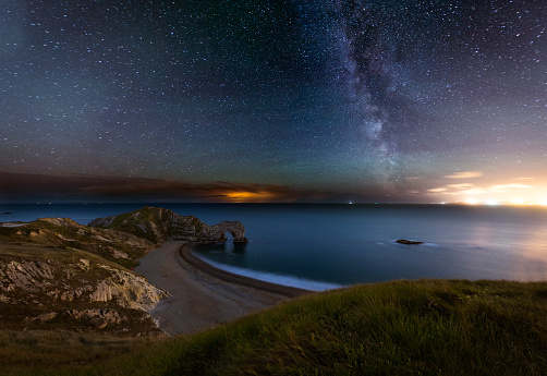 A night photograph taken at Durdle Door in Dorset. One of the most recognizable landmark in the UK. The photograph is taken at the waters edge and shows crashing waves, curve of the beach and the famous arch way. You can also see the Milkway.