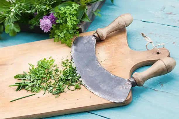 chopper with cutted herbs on a wooden cutboard and a wooden tray with fresh herbs