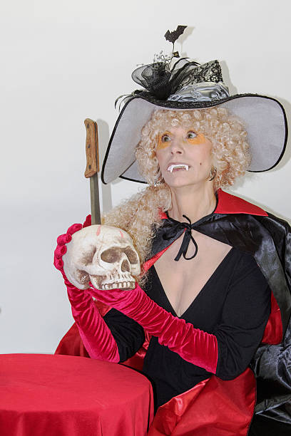 Fanged Witch Holding Skull This fanged witch has just plunged this butcher knife into the skull and is holding up her feat for all to see fanged stock pictures, royalty-free photos & images