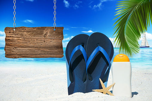 Flip Flops, suntan lotion and wooden signboard with copy space on the beach