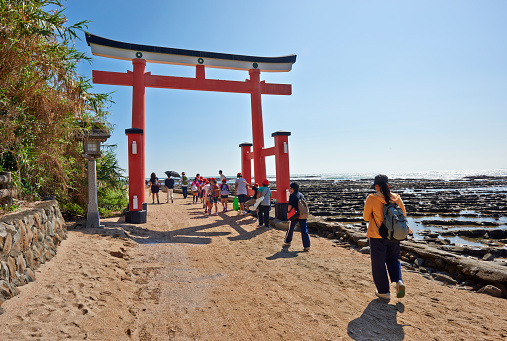 Aoshima, Japan - September 26, 2014: A schoolchildren group and tourists walking through a torii gate at the entrance of Aoshima Island. The island is a popular tourist destination in Miyazaki Prefecture.