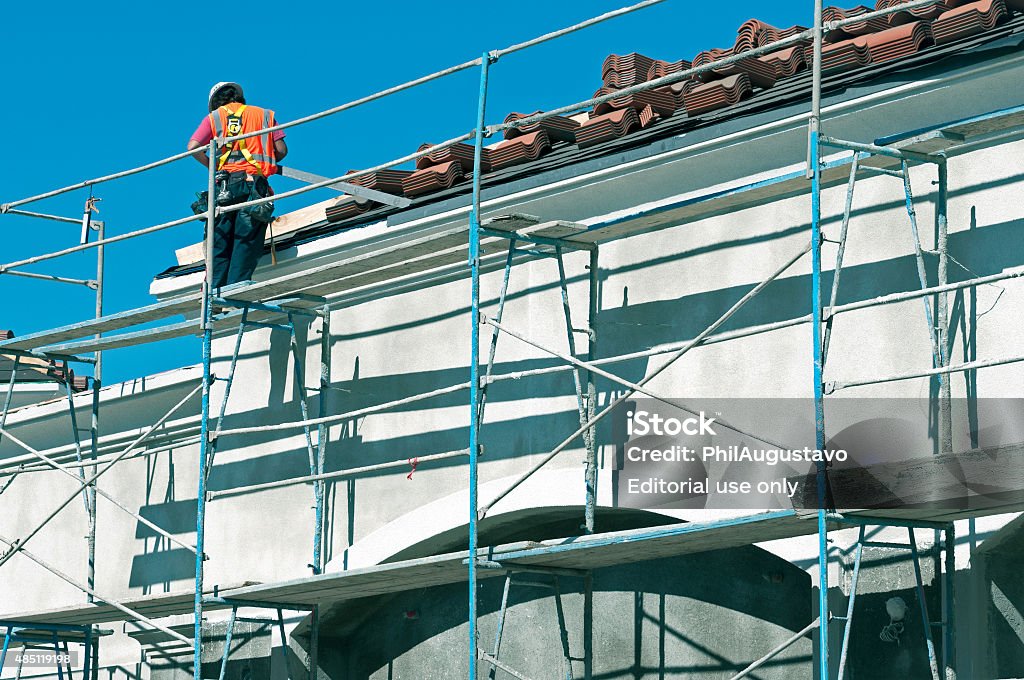 Worker protecting wall with flashing in California Cabazon, California, USA--February 24, 2014: A construction worker prepares to fit a piece of metal flashing to the edge of a rooftop at a site in Cabazon CA in winter. Office Building Exterior Stock Photo