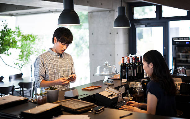 Young adult paying at a restaurant Young good-looking asian guy is paying for his order at the bar counter. japan restaurant bill stock pictures, royalty-free photos & images