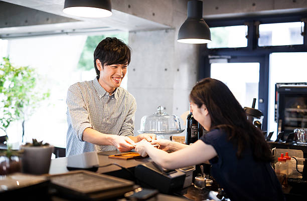 Asian guy paying in a cafe Young handsome adult guy is paying for food for the cashier at a bar counter. Both people are in positive emotion. japan restaurant bill stock pictures, royalty-free photos & images