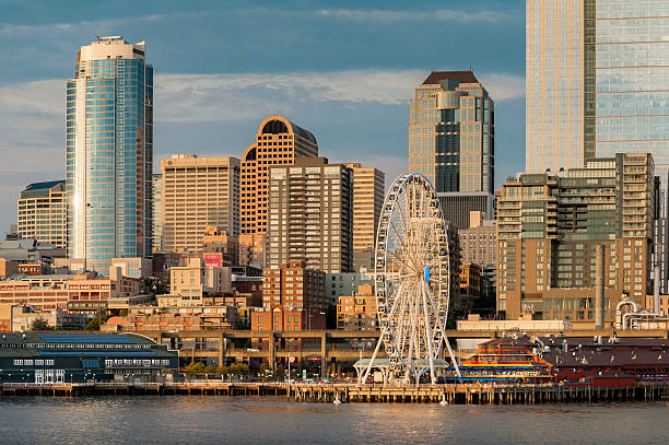 Seattle Waterfront Modern office buildings and a Ferris Wheel dominate the exciting and vibrant Seattle, Washington waterfront during a lovely summer sunset. great ferris wheel puget sound seattle washington pier amusement ride stock pictures, royalty-free photos & images