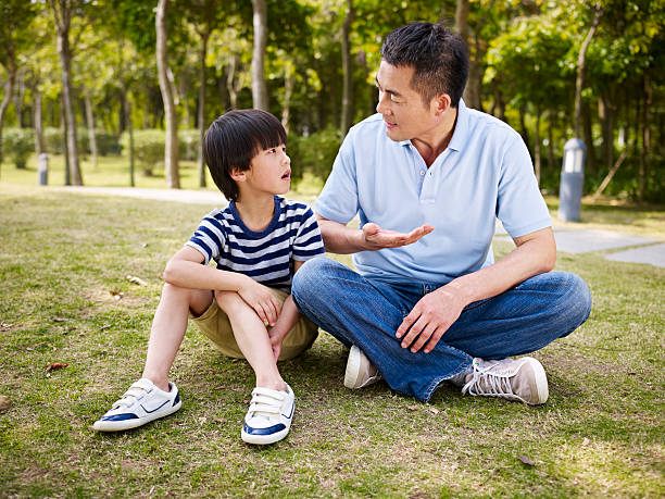 asian father and son having a conversation asian father and elementary-age son sitting on grass outdoors having a serious conversation. child japanese culture japan asian ethnicity stock pictures, royalty-free photos & images