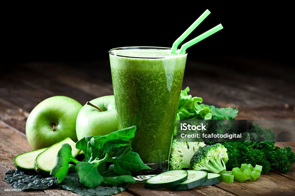 Green vegetable juice on rustic wood table Glass of fresh green vegetable juice with two drinking straws on rustic wood table. The glass is surrounded by green vegetables like spinach, lettuce, broccoli, celery, green apples, parsley and cucumber. This is a drink used for detox diet. Predominant colors are green and brown.  DSRL studio photo taken with Canon EOS 5D Mk II and Canon EF 70-200mm f/2.8L IS II USM Telephoto Zoom Lens Smoothie Stock Photo